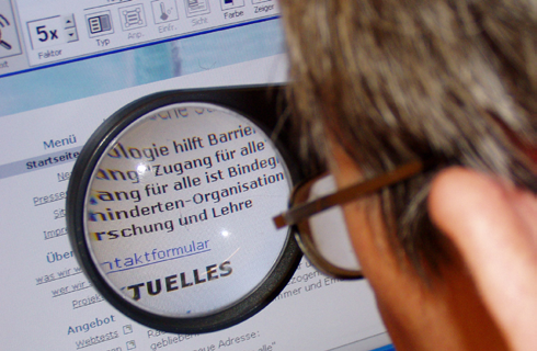 Partially sighted person looking at a computer screen through a magnifying glass�